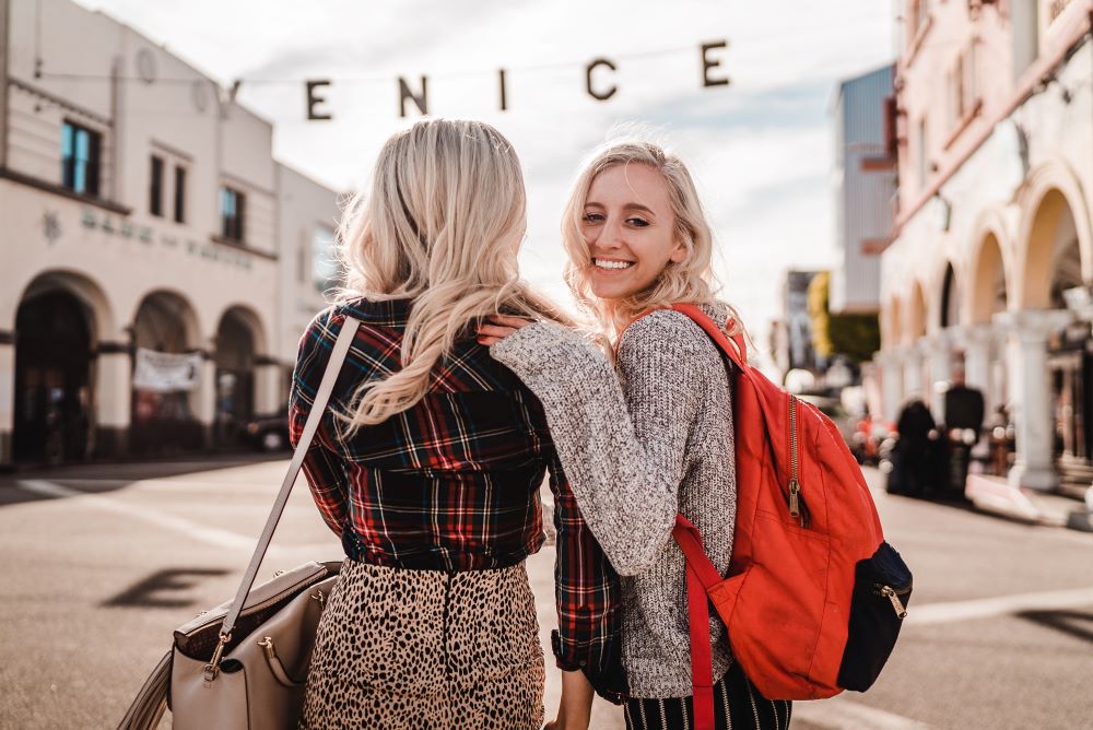 two women standing in front of venice sign and one woman with hand on the other's shoulder while smiling at camera