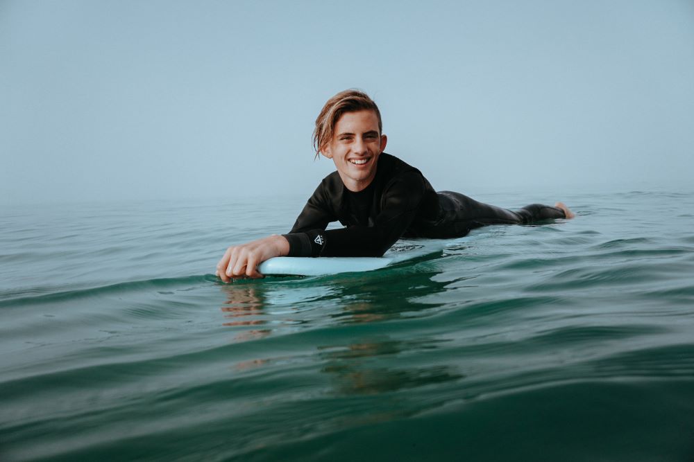 young male laying on surfboard smiling